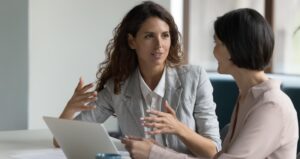 Two professional women are engaged in a discussion at a modern office setting. 