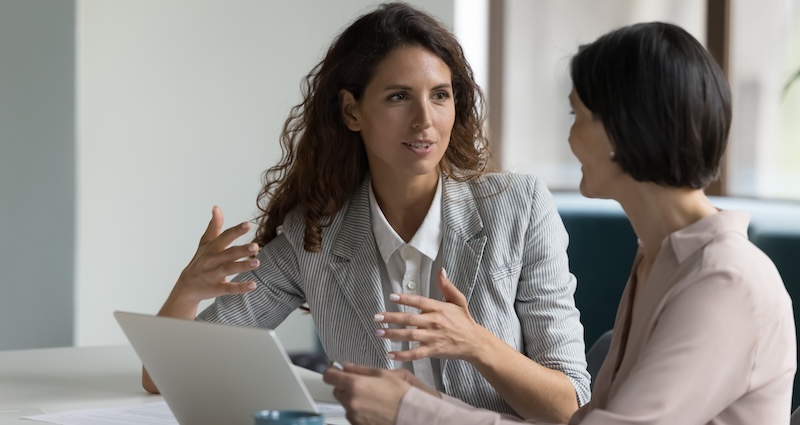 Two professional women are engaged in a discussion at a modern office setting.